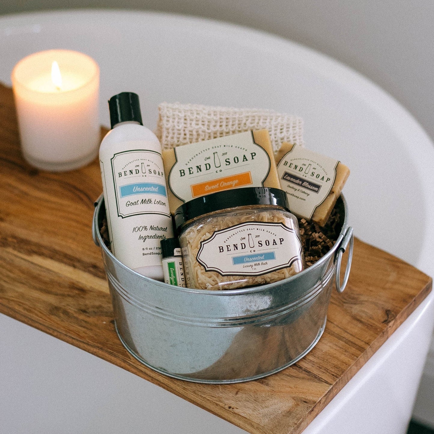 Skincare bundle in a silver tin, including goat milk soap, goat milk lotion, lip butter, and loofah